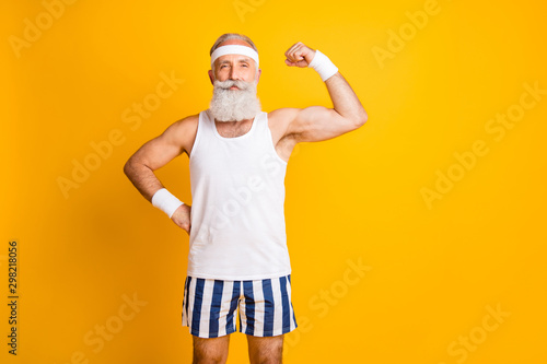 Photo of cheerful positive attractive handsome old man demonstrating his muscles looking intently at you holding hand on waist isolated vivid color yellow background