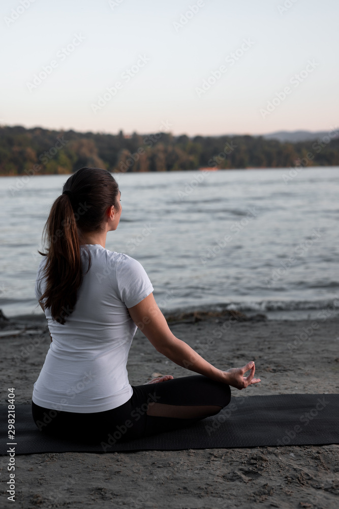 Beautiful young woman is practicing meditation on the river bank