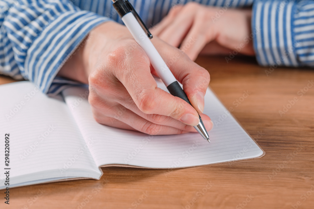 Beautiful Female hands write pen in a notebook of tasks and goals to work on a wooden table Beautiful Female hands write pen in a notebook of tasks and goals to work on a wooden table