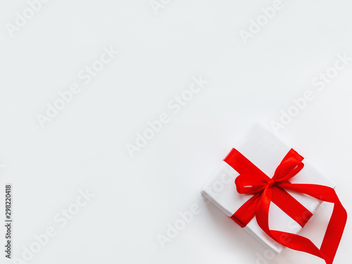 Present in white wrapping paper on white backdrop. Holiday gift with red ribbon and bow. Copy space.