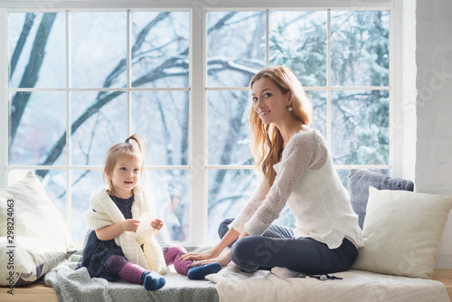 Mother and daughter in the living room sits on the window sill in winter morning