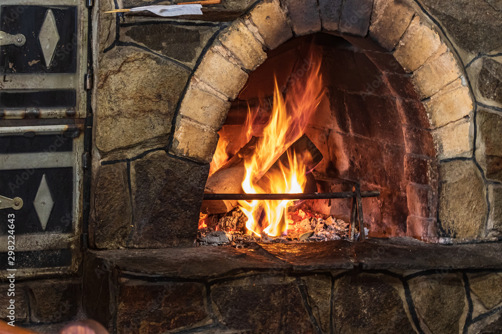 Arched fireplace with blazing fire. Photo with a beautiful traditional stone fireplace with firewood and a place for advertising or a greeting lettering on a dark background.