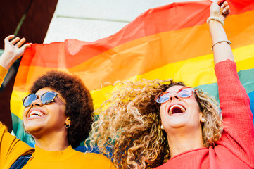 Two women friends hanging out in the city waving LGBT with pride flag