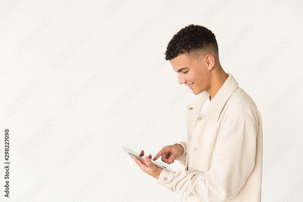 Smiling young man using tablet computer. Side view of cheerful young man using digital tablet isolated on grey background. Wireless technology concept Smiling young man using tablet computer. Side view of cheerful young man using digital tablet isolated on grey background. Wireless technology concept