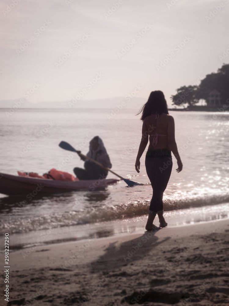 Silhouette of Woman Walking on Sunny Beach with Kayaker Nearby