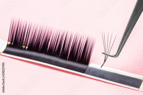 Bunches of fake lashes and tweezers on pink background. Eyelash extension procedure