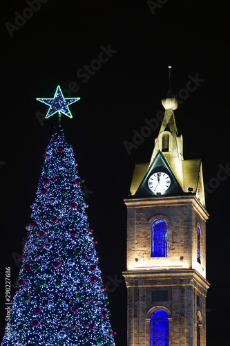 Blue Christmas tree with a blue star next to the chapel and the clock on the tower on the background of the night sky. New Year tree with a chapel on a black background. photo