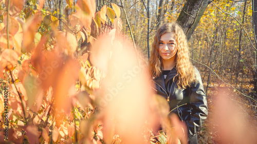 Beautiful woman looking out from behind tree. Pretty calm woman touching tree and looking at camera in quiet forest