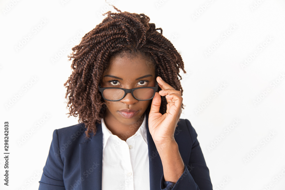 Serious office worker taking her glasses off. Young African American business woman looking at camera over eyeglasses. Isolated front over white background Vision concept Serious office worker taking her glasses off. Young African American business woman looking at camera over eyeglasses. Isolated front over white background Vision concept