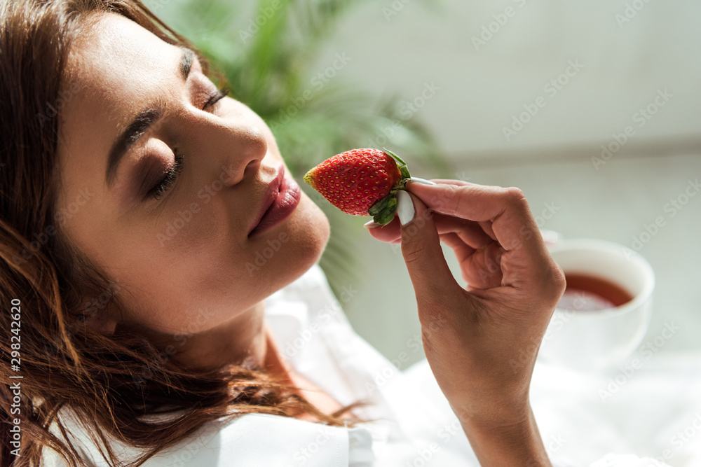 attractive woman with closed eyes holding strawberry at morning attractive woman with closed eyes holding strawberry at morning