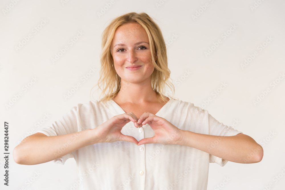 Content woman showing hand heart gesture. Portrait of beautiful cheerful young woman showing heart symbols with fingers and smiling at camera. Gesture concept Content woman showing hand heart gesture. Portrait of beautiful cheerful young woman showing heart symbols with fingers and smiling at camera. Gesture concept