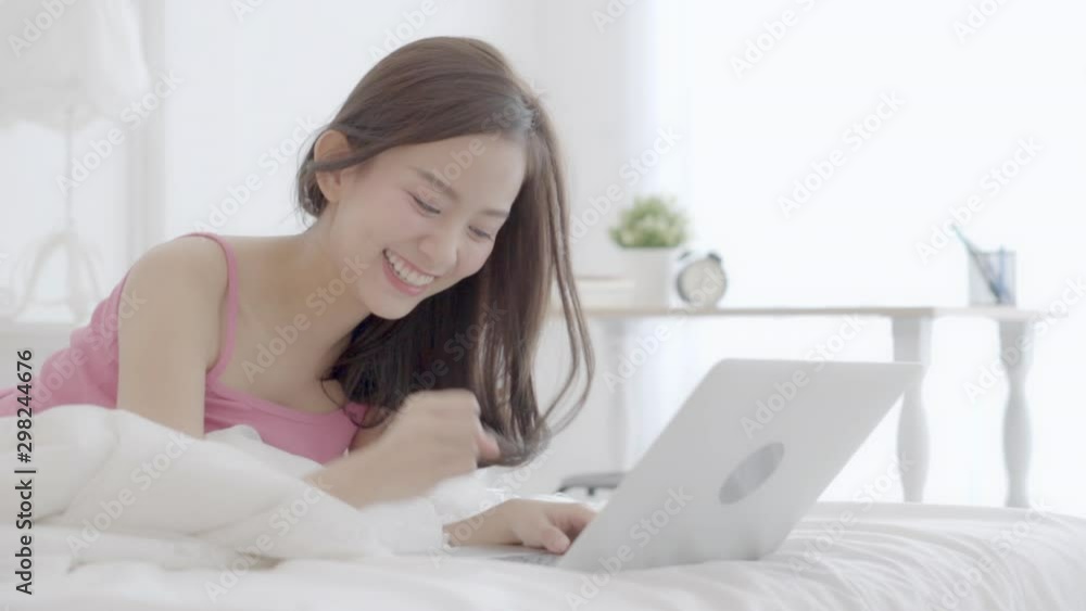 Beautiful asian young woman smiling lying on bed using laptop computer with success at bedroom, freelance with girl happy working notebook excited, communication and lifestyle concept. Beautiful asian young woman smiling lying on bed using laptop computer with success at bedroom, freelance with girl happy working notebook excited, communication and lifestyle concept.