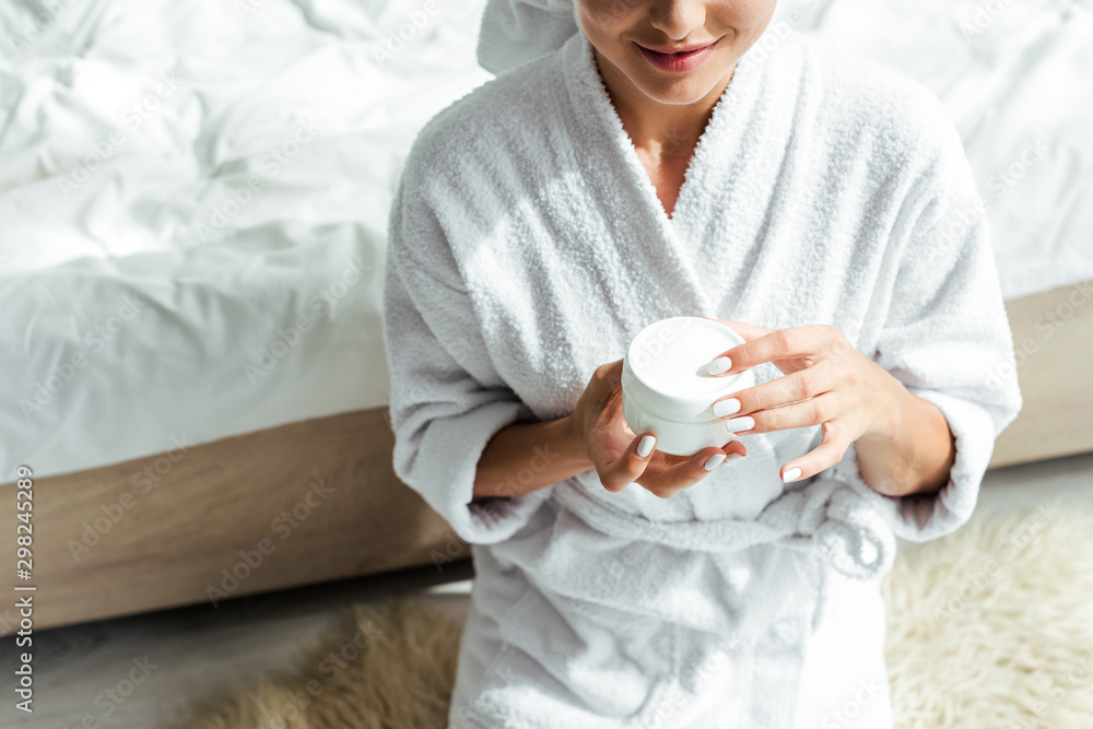 cropped view of woman in bathrobe holding cosmetic cream at morning cropped view of woman in bathrobe holding cosmetic cream at morning