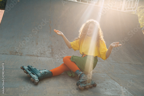 Young woman girl in green and yellow clothes and orange stockings with curly hairstyle roller skating fell in skate park