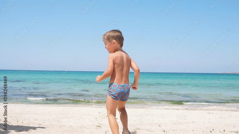 Happy little boy runs along the beach towards the sea. Active rest and relaxation in the sun and sea Happy little boy runs along the beach towards the sea. Active rest and relaxation in the sun and sea