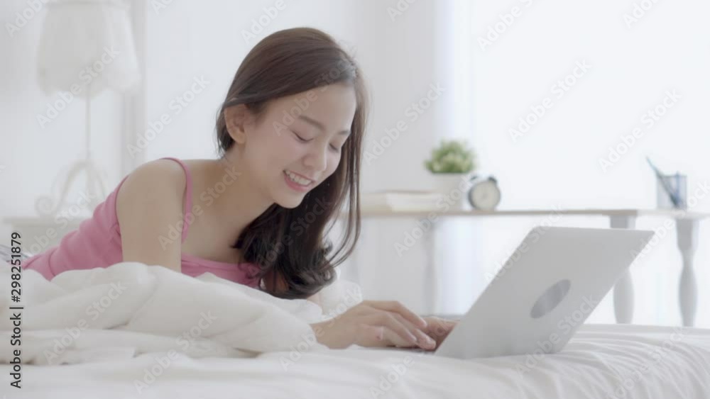 Beautiful asian young woman smiling lying on bed using laptop computer at bedroom for leisure, freelance with girl happy working notebook, communication and lifestyle concept. Beautiful asian young woman smiling lying on bed using laptop computer at bedroom for leisure, freelance with girl happy working notebook, communication and lifestyle concept.