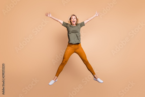 Full length photo of crazy funky lady jumping high making star shape figure spending best free time wear green t-shirt yellow trousers sneakers isolated beige color background
