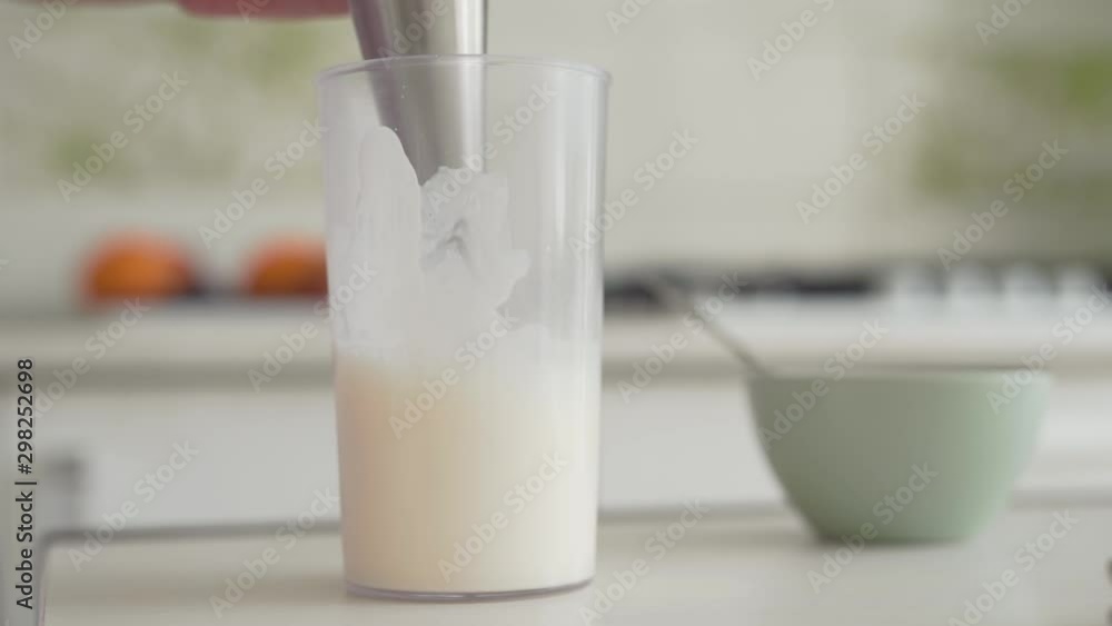 Electric mixer beating cream in glass on kitchen table top close up Electric mixer beating cream in glass on kitchen table top close up