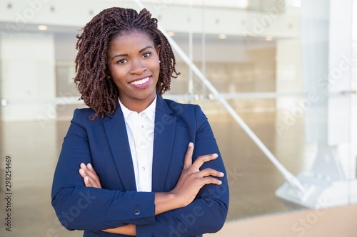 Happy successful professional posing near office building. Young African American business woman with arms folded standing outside, looking at camera, smiling. Female business leader concept