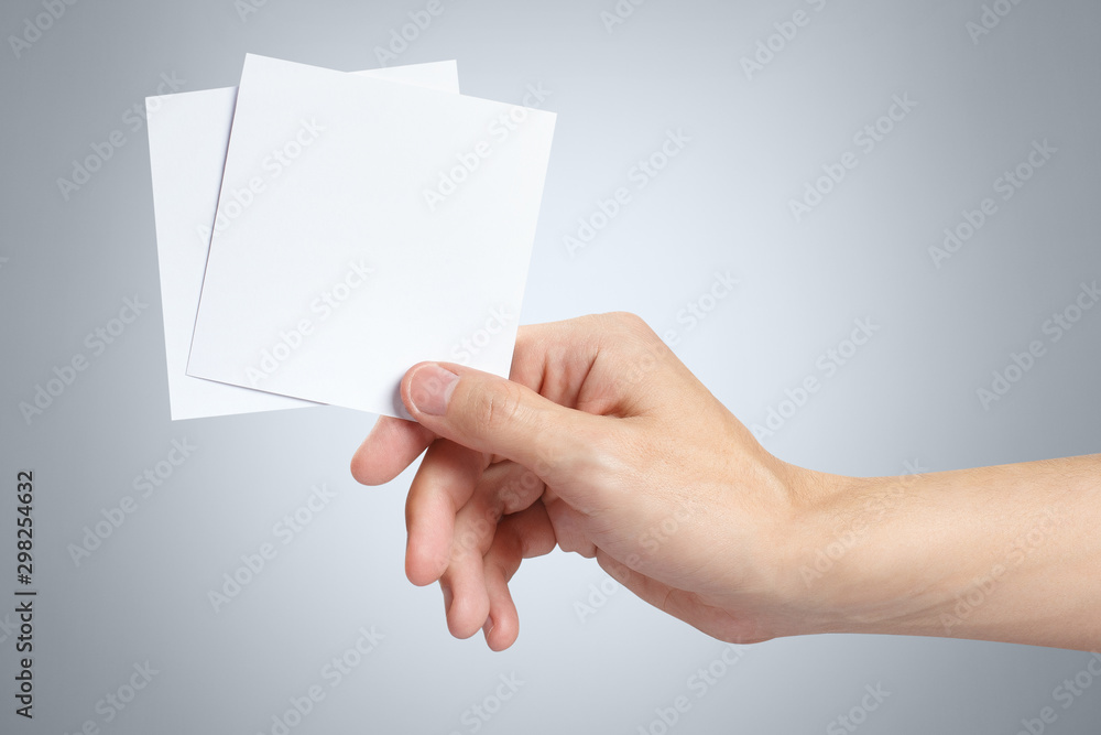 Male hand holding two square blank sheets of paper (tickets, flyers, invitations, coupons, etc.) on gray background