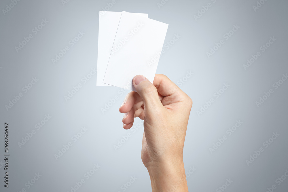 Hand holding two small pieces of paper or plastic (cards, tickets, flyers, invitations, coupons, banknotes, etc.) on gray background Hand holding two small pieces of paper or plastic (cards, tickets, flyers, invitations, coupons, banknotes, etc.) on gray background