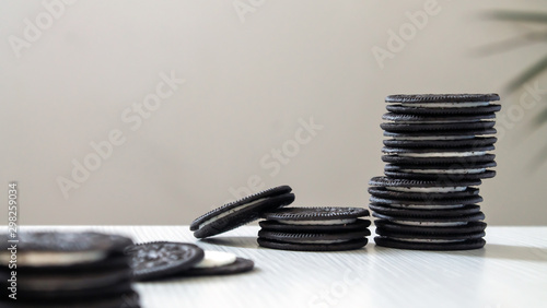 black cookies standing pinnacle with white cream center on a white wooden background with palm leaves behind.