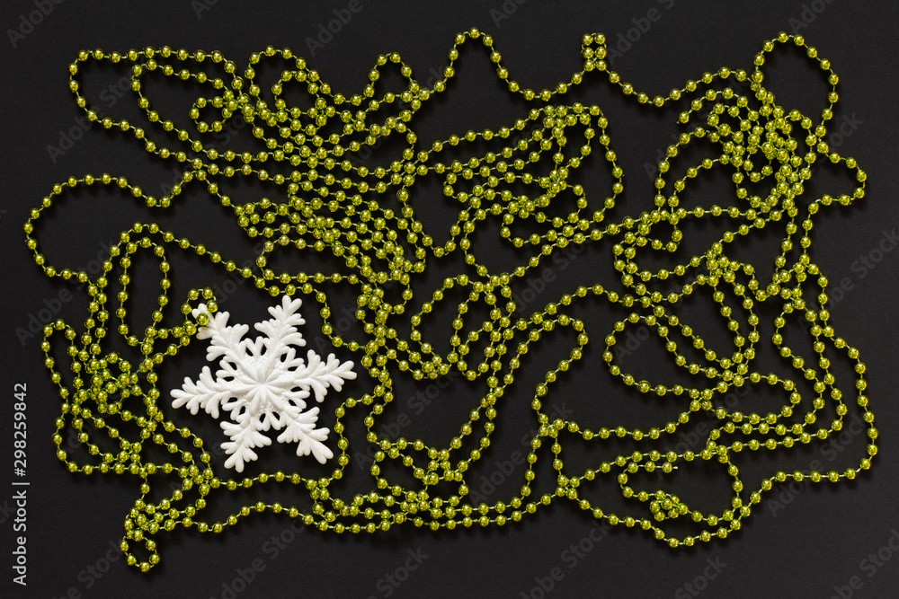 Holiday background , white snowflake and green bright decorative beads on black background, flat lay, top view