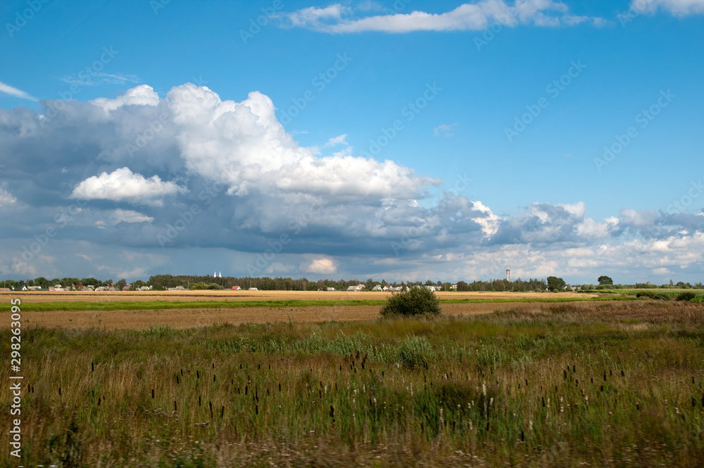 Rural Lithuania, rural scene across field to village with cloud formation