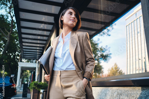 Εκτύπωση καμβά Young attractive stylish businesswoman with laptop happily looking away on stree