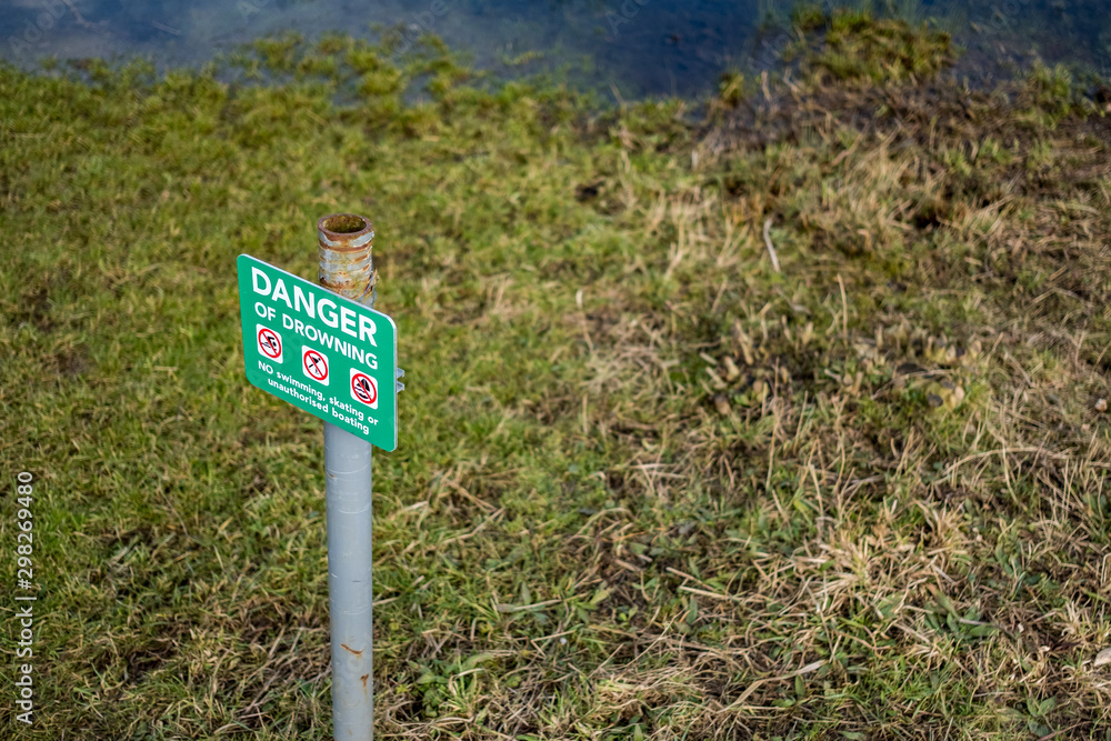 Obraz premium Metal Danger of Drowning sign seen positioned near a large inland water in England. Seen adjacent to reeds, the image was taken at sunset.
