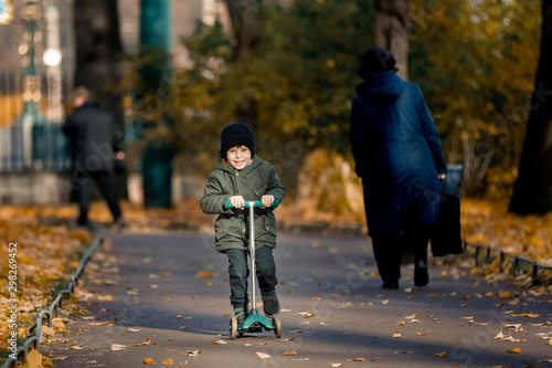 child riding a scooter. The boy rides in the autumn park on a scooter in a hat and jacket