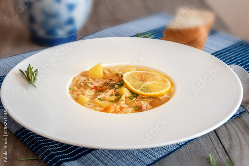 Delicious low-calorie chicken soup with small noodles and vegetables in a white round plate on the table