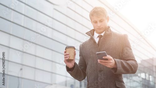 Portrait of handsome business man using smartphone and drinking coffee in the city.