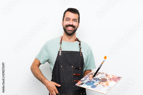 Young artist man holding a palette over isolated background laughing