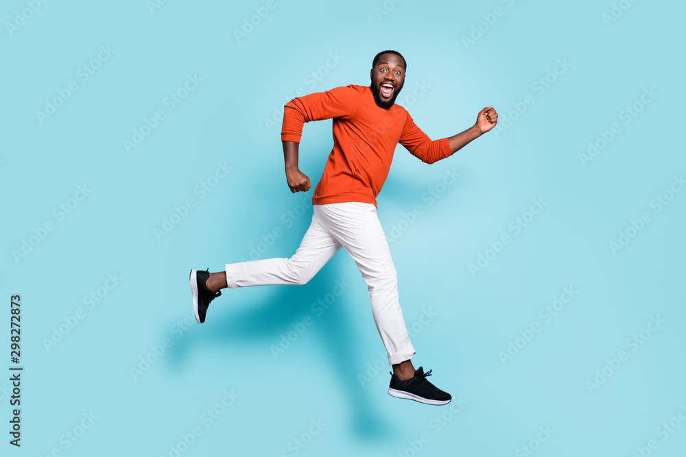 Full length body size photo side profile of man mixed-race expressing positive emotions wearing sneakers white trousers pants running jumping to discounts isolated vivid blue color background Full length body size photo side profile of man mixed-race expressing positive emotions wearing sneakers white trousers pants running jumping to discounts isolated vivid blue color background