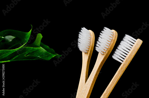 Bamboo toothbrushes with green leaves on black background.