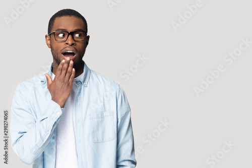 Shocked African American man in glasses covering mouth, looking aside