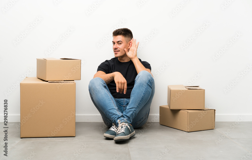 Handsome young man moving in new home among boxes listening something Handsome young man moving in new home among boxes listening something