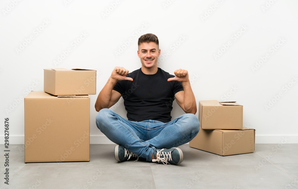 Handsome young man moving in new home among boxes proud and self-satisfied Handsome young man moving in new home among boxes proud and self-satisfied