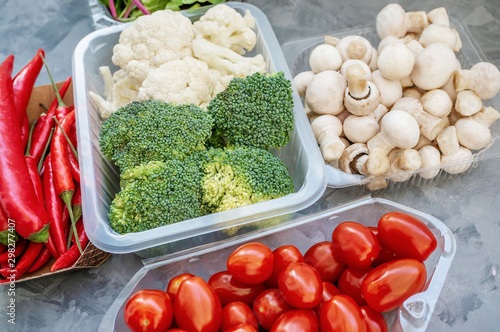 Mixed cauliflower and broccoli vegetables, baby salad, mushrooms, peppers, tomatoes and chili in lunch box on wooden background in rustic style photo