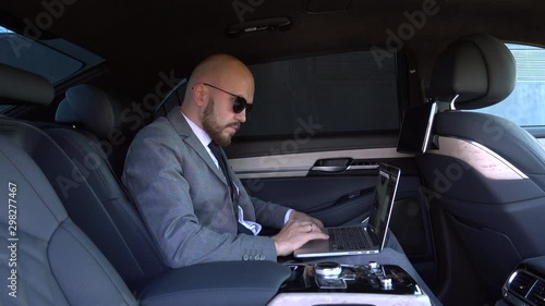 Handsome businessman sitting with laptop on the backseat of the car. travelling by a car and working on laptop computer