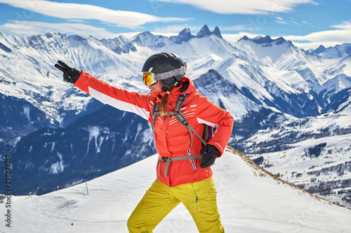 Obraz na płótnie Woman skier smiling and posing at Les Sybelles ski domain, with Aiguilles d'Arves peaks in the background, on a sunny day with blue skies. w salonie