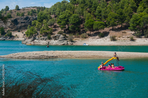 People swimming and relaxing on a lake with rocky shore. Sunny day on a lake with turquoise water. Summer vacations. Water reservoir in Spain.