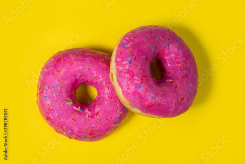 Two sweet pink donuts isolated on yellow background. Bright tasty bun. Minimal summer concept. Flat lay. The concept of unhealthy eating and weight gain. Harmful fast food