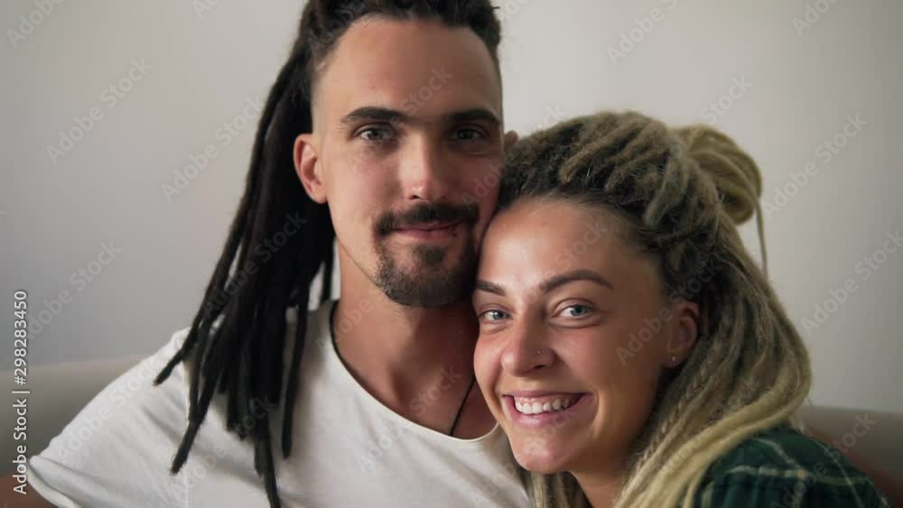 Close up portrait of the young dreadlock couple in love looking directly to the camera and smiling on the white background wall. Indoors Close up portrait of the young dreadlock couple in love looking directly to the camera and smiling on the white background wall. Indoors