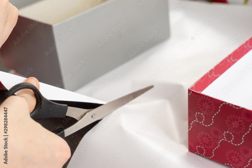 Person using scissors to cut a roll of plain white wrapping paper