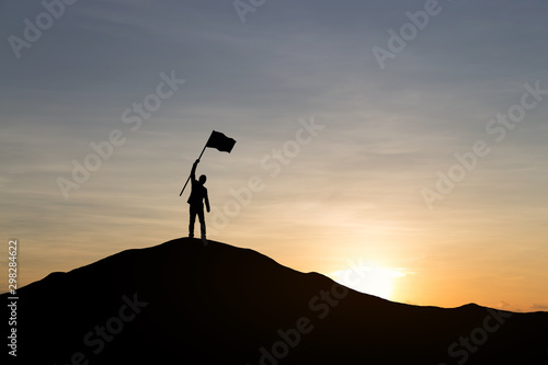 Silhouette of businessman holding a flag on top mountain, sky and sun light background. Business success and goal concept.