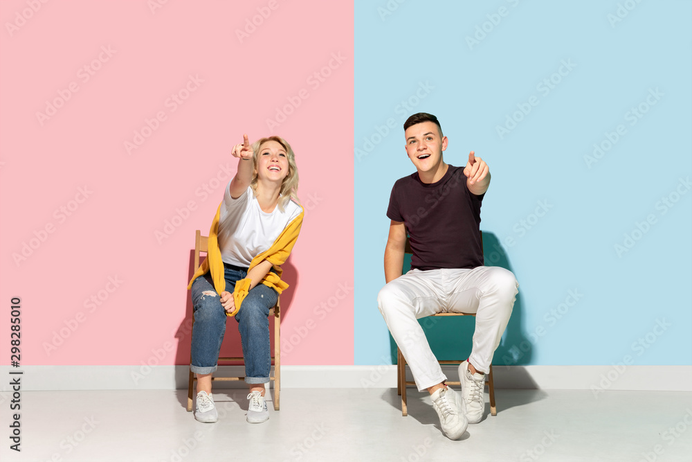 Young emotional man and woman in bright casual clothes posing on pink and blue background. Concept of human emotions, facial expession, relations, ad. Beautiful caucasian couple pointing dreamful.
