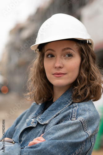 Portrait of a beautiful young female factory worker wearing a white safety helmet and posing outdoors with crossed arms © cineberg