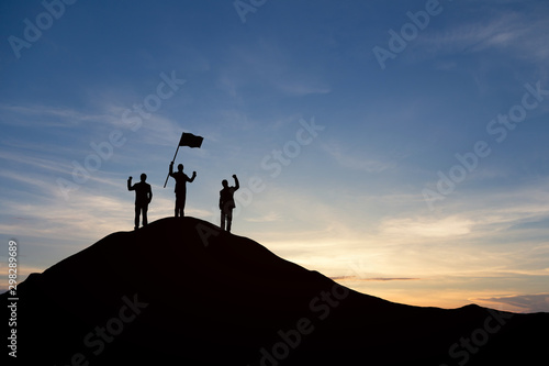 Silhouette of people are celebrating success at the top of the mountain, sky and sun light background. Team business concept. © cofficevit